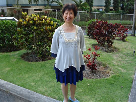 A cheerful woman poses in a garden surrounded by vibrant plants on a sunny afternoon.