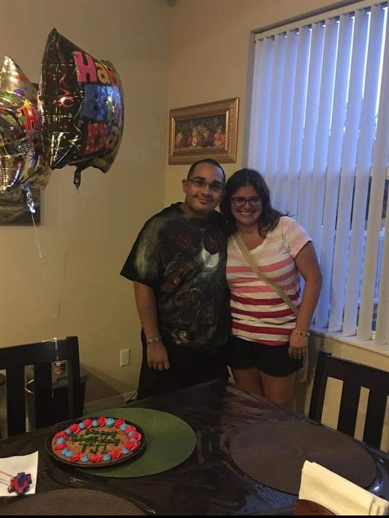 Two friends pose happily together near a decorated table with a cake while balloons float nearby.