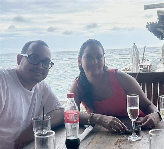 Two friends relax at a seaside table while sipping drinks, enjoying the ocean view at dusk.
