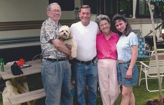 A cheerful family stands together with their dog, enjoying a sunny summer day outdoors.