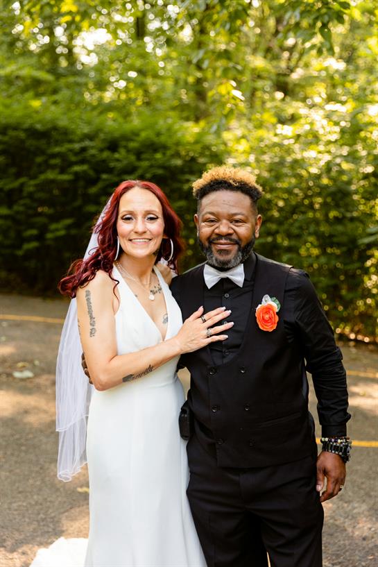 Joyful couple poses together in formal attire, celebrating their wedding amidst vibrant foliage.