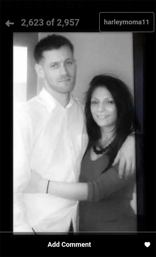 A couple stands close together, sharing a warm embrace while smiling at the camera in soft lighting.