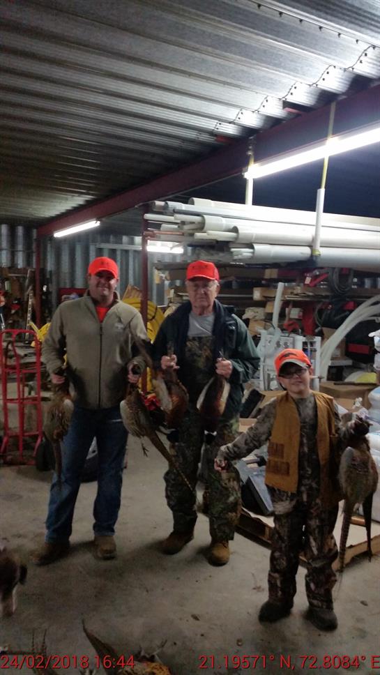 Three generations of hunters proudly display their pheasant catch in a garage.