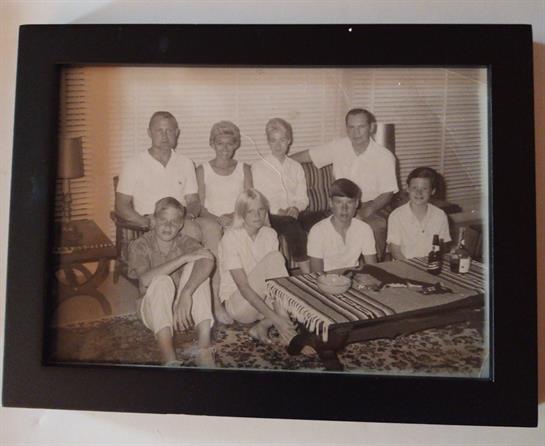 Group of eight people smiling and relaxing in a living room with casual attire and drinks.