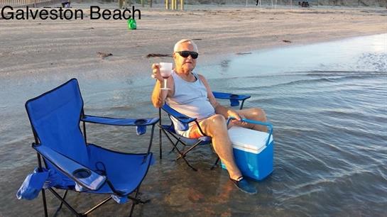 Elderly man enjoys a cold drink while sitting in shallow water at the beach during evening hours.