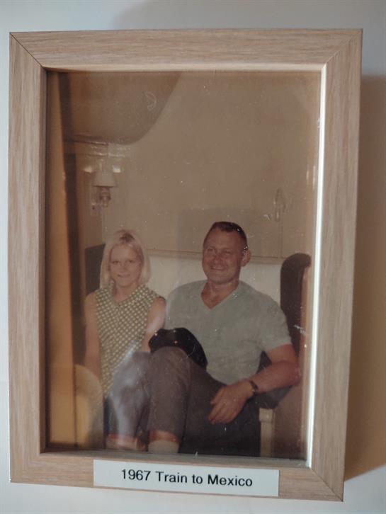 Two people sit closely together, smiling warmly in a cozy room filled with soft furnishings.