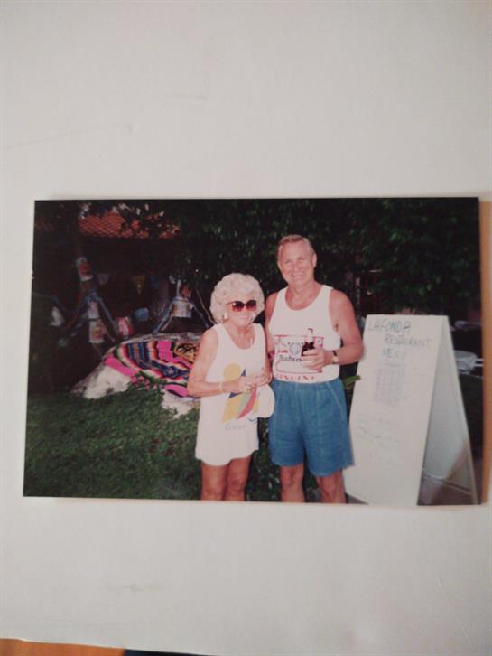 A cheerful couple enjoys refreshments in a lively garden, surrounded by colorful decorations.