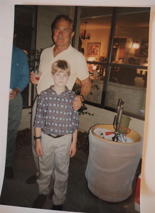 A young boy poses next to an adult man at an indoor gathering in the evening.