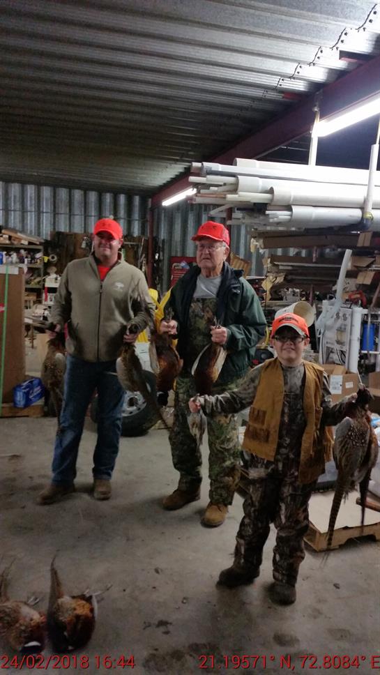 Three hunters, including a child, hold up their catch of the day in an indoor shed.