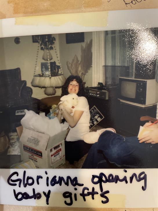 A woman smiles as she opens gifts while sitting in a living room filled with holiday decorations.