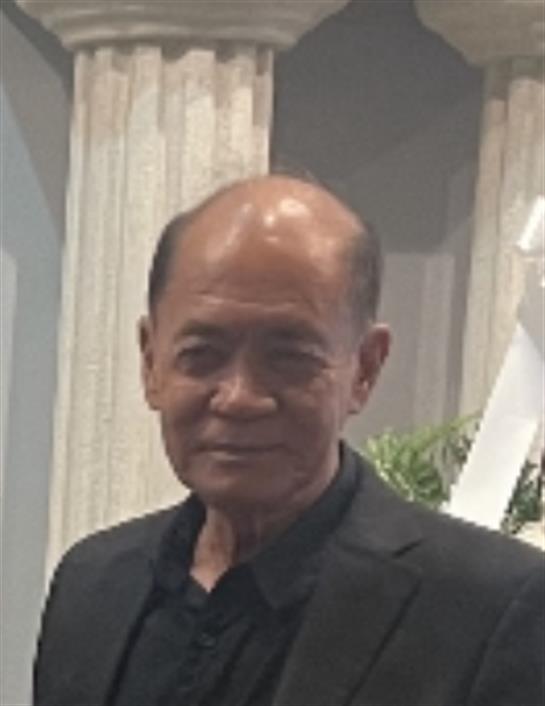 An elderly man in formal attire poses confidently in a stylish indoor setting with decor.