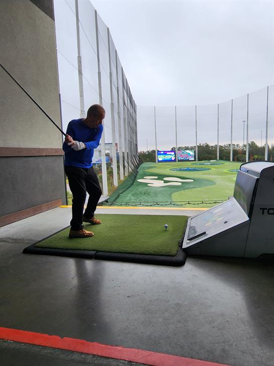Golfer focuses on improving swing form at a driving range with a tech-enabled mat and screen.