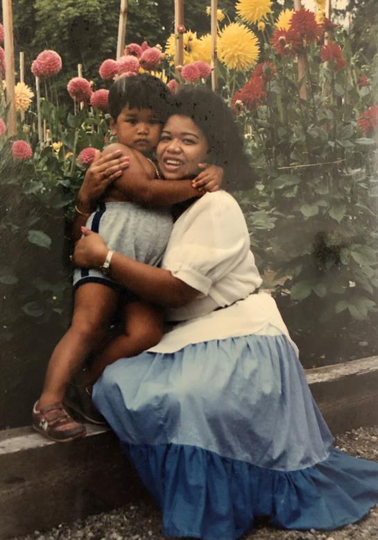 A joyful mother holds her child among vibrant rose bushes on a sunny day.