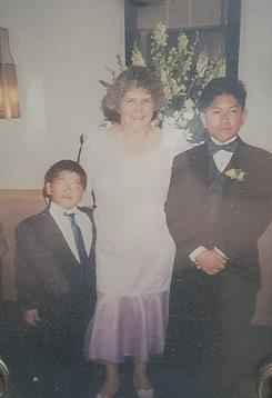Two boys in suits and an adult in a gown pose together at a festive event with decorations.