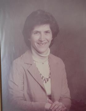 A woman poses for a portrait wearing a pink blazer and necklace, smiling warmly.