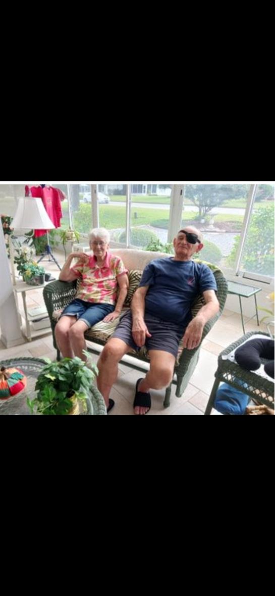 Two seniors relax on a cozy couch, enjoying each other's company in a bright, green room.