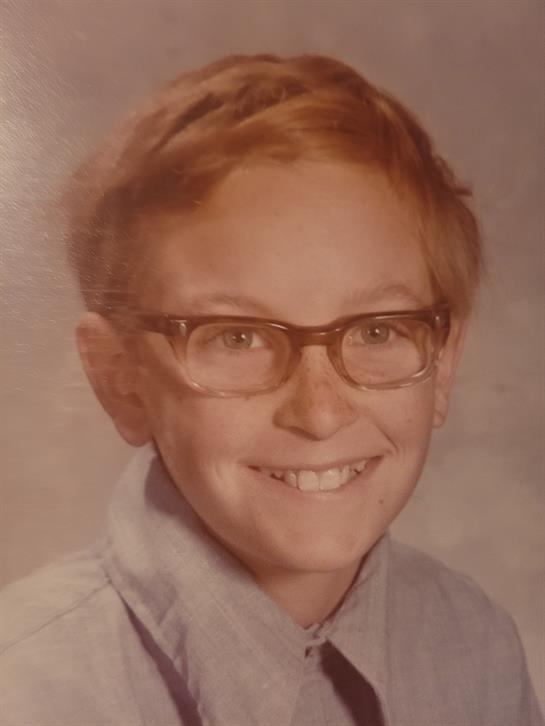 A cheerful young boy wearing glasses shows a bright smile while posing for a school portrait.