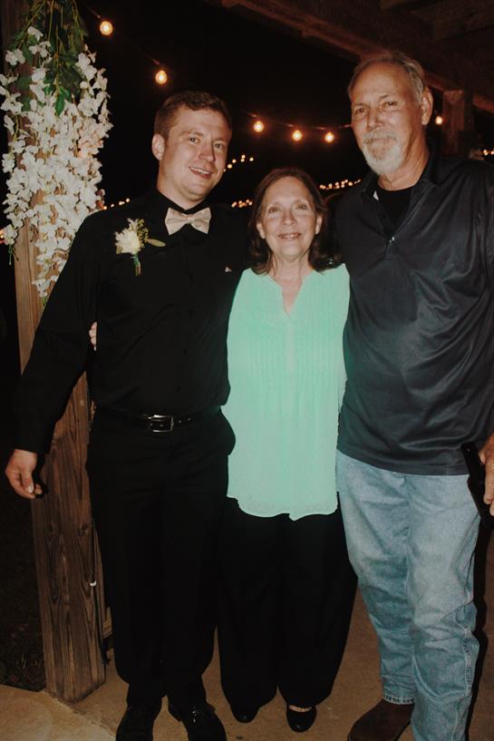 Three family members stand together smiling at a joyful gathering under string lights.