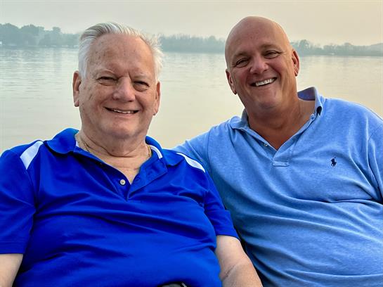 Two men share a joyful moment by the water, enjoying a peaceful sunset together with big smiles.