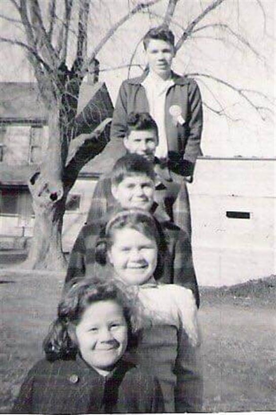 Children smile and pose in a playful line outside, enjoying a sunny day in the park during spring.