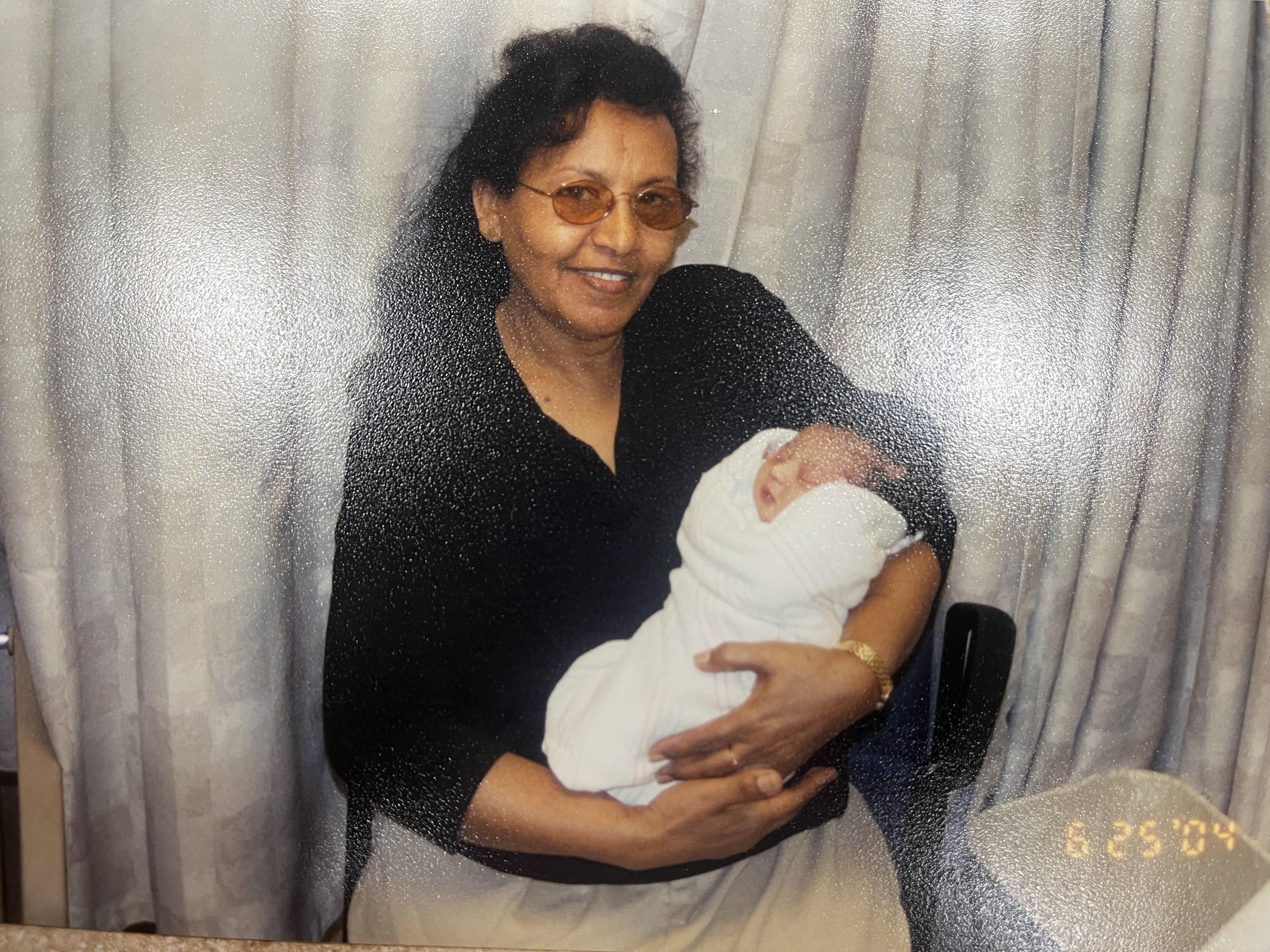 A grandmother lovingly holds her newborn grandchild in a warm, inviting indoor space.