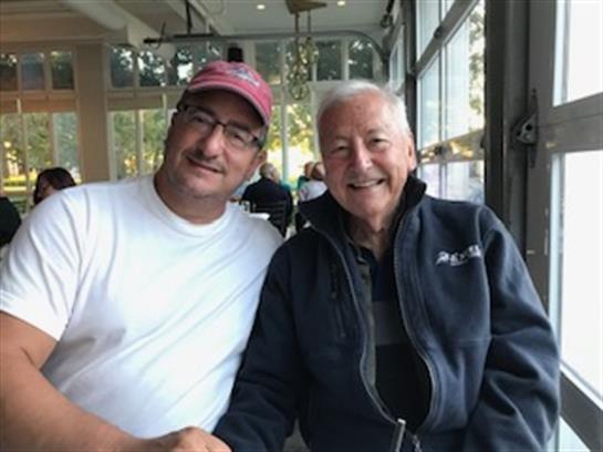 Two friends smile while seated at a cafe, sharing a warm moment during a sunny afternoon.