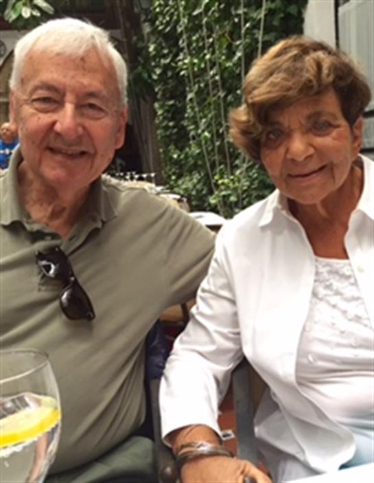 Senior couple sits close, smiling and enjoying refreshing drinks while relaxing outdoors.