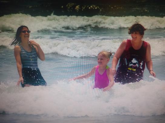 Three people laugh and play in the ocean waves while enjoying a sunny beach day.