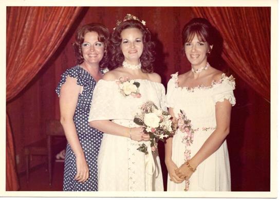 Three women pose together in beautiful dresses, celebrating a joyful event in the 1970s.