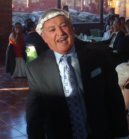 A man wearing a suit performs joyfully at a lively indoor event with guests celebrating around.