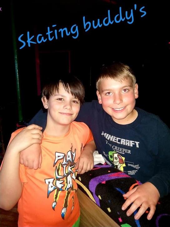 Two young boys smile for the camera at a fun skating rink night with friends.