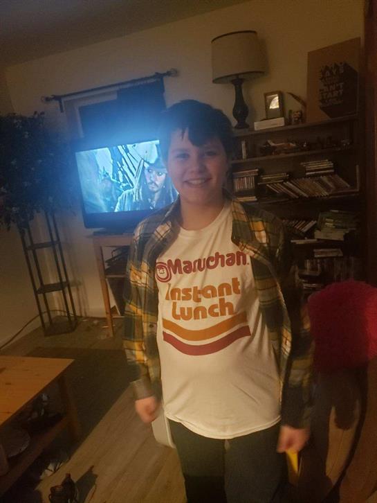 A young person smiles confidently in a living room, dressed casually.