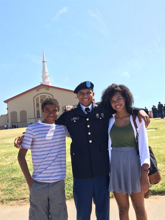 Family members pose together joyfully after attending a military graduation ceremony outdoors.
