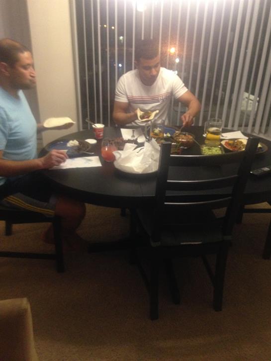 Two friends share a meal at a round dining table while enjoying each other's company in the evening.