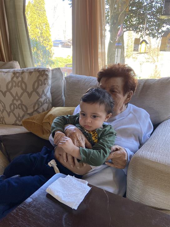 A toddler sits in the lap of a woman on a comfortable couch in a bright afternoon setting.