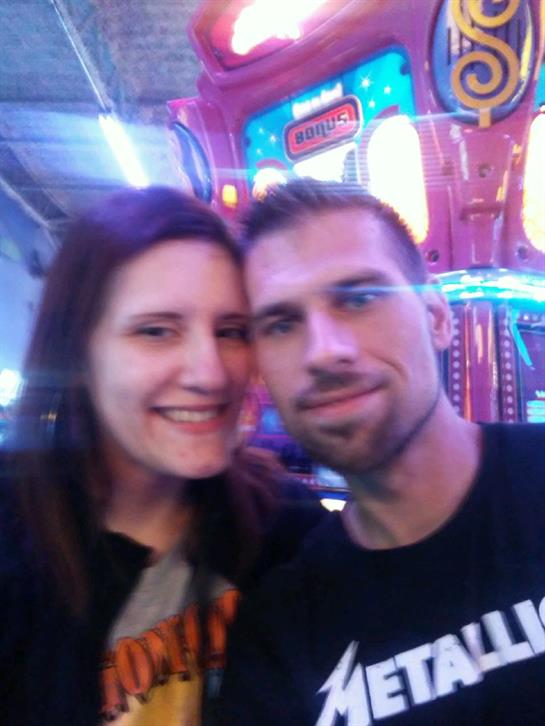 A joyful couple poses for a selfie at an amusement arcade filled with bright lights and games.