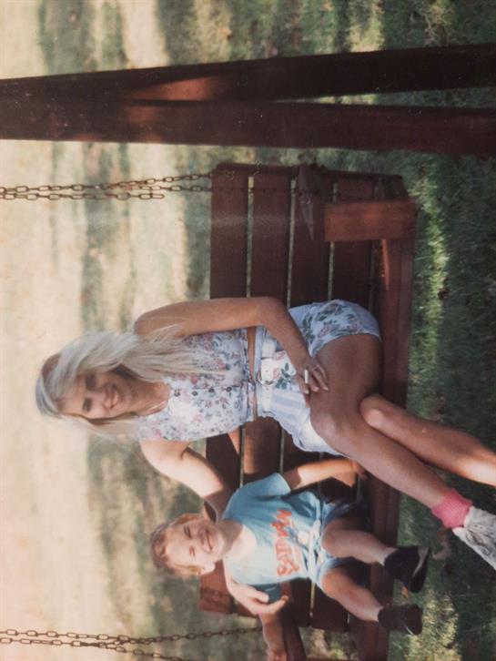 A woman and a young boy relax on a swing, enjoying the pleasant weather in a park.