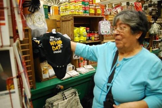 An elderly woman enjoys shopping at a store, holding up a playful baby onesie to explore its design.