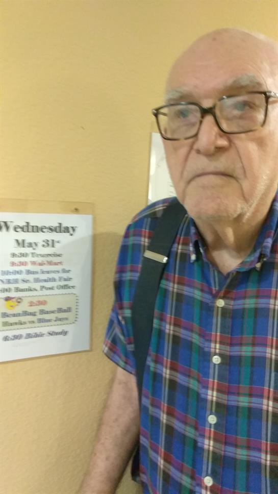 A senior man with glasses is next to a schedule for activities at a community center.