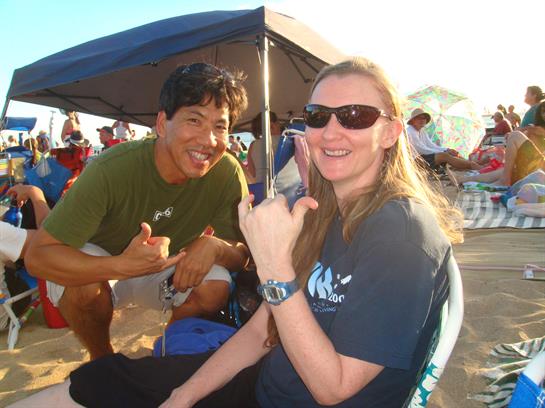 Two friends pose happily under a tent during a beach gathering in Hawaii, radiating joy and warmth.