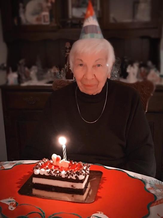 An old woman sitting at a table with a birthday cake