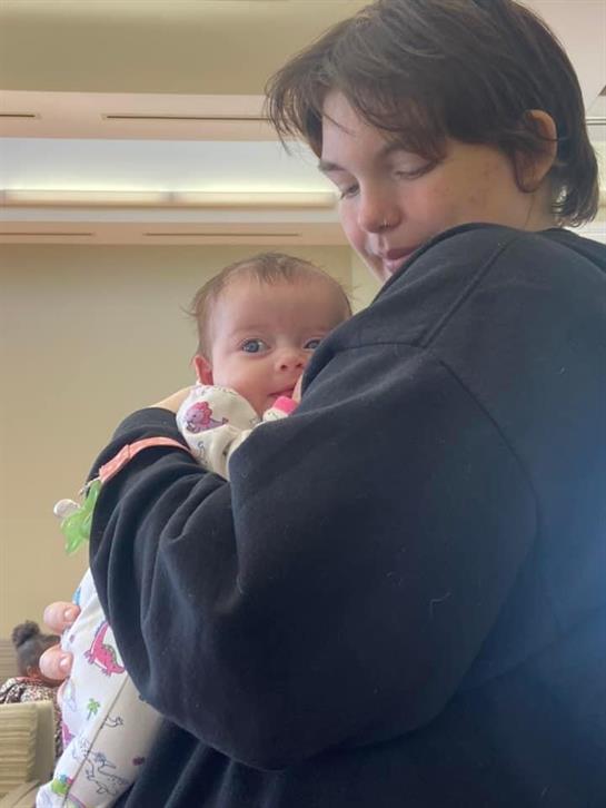 A smiling baby is cradled by a caregiver in a cozy indoor environment surrounded by soft colors.