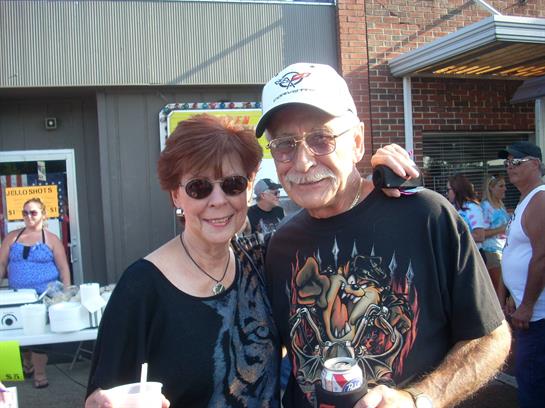 A couple poses together at a vibrant outdoor event, enjoying refreshments and each other's company.
