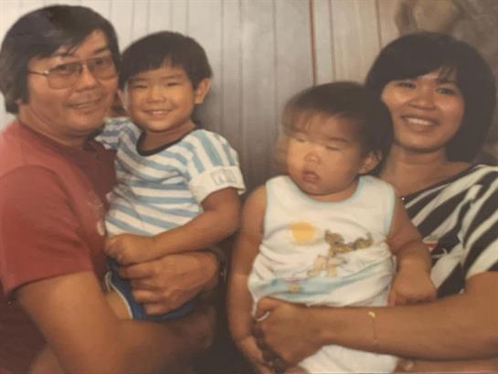Two parents hold their children in a warm, intimate indoor space, sharing a joyful moment together.