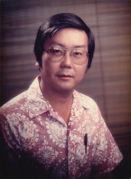 A man in a floral shirt and glasses poses indoors, exuding a calm and approachable demeanor.