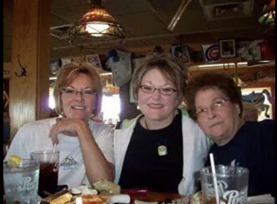 Three friends sit together at a table, smiling and sharing a meal in a warm restaurant atmosphere.
