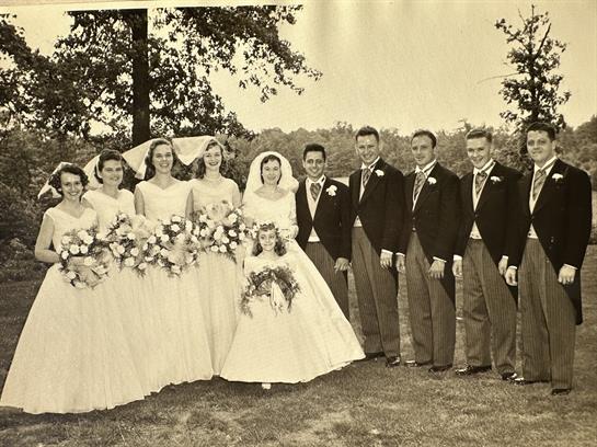Bridal party stands in a lush outdoor setting wearing elegant gowns and suits, radiating happiness.