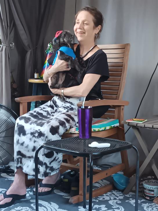 A woman relaxes in a chair, holding her small dog, enjoying an outdoor afternoon with beverages.