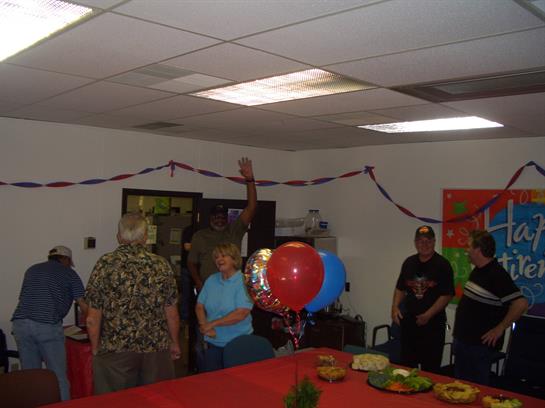 People are celebrating in a decorated office with food, balloons, and a festive atmosphere.