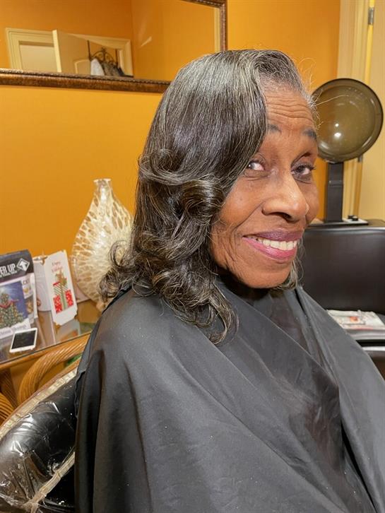 A joyful woman sits in a salon chair, preparing for a hairstyle amidst modern decorations.